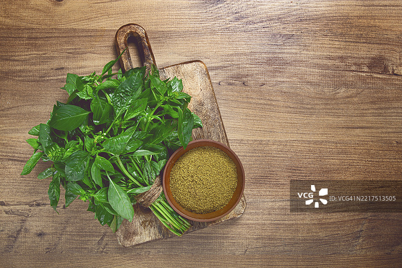 绿色罗勒碎放在陶瓷碗中，旁边是一束新鲜的绿色罗勒，桌子上俯视图，无人。图片素材
