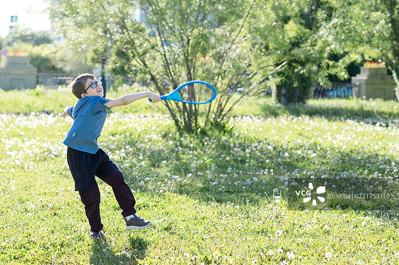 一个11岁的小男孩戴着阅读眼镜和助听器，在公园的绿草坪上打沙滩网球。图片素材