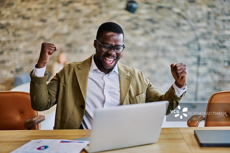 兴奋的商人在办公室用笔记本电脑庆祝成功图片素材