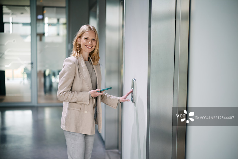 女商人一边拿着智能手机一边按电梯按钮图片素材