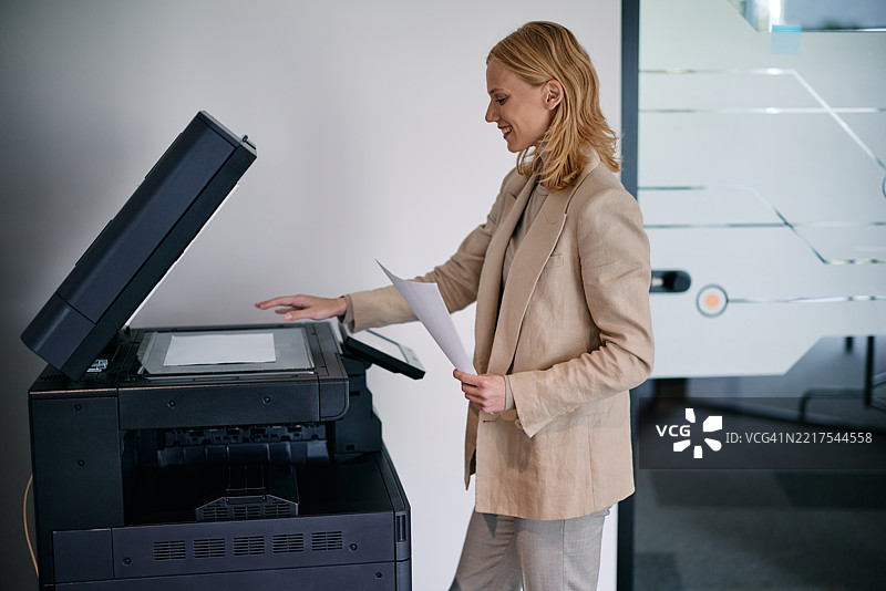 女商人在办公室使用现代多功能打印机复印文件图片素材