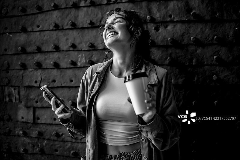 快乐的女人微笑着，手里拿着咖啡杯和手机图片素材
