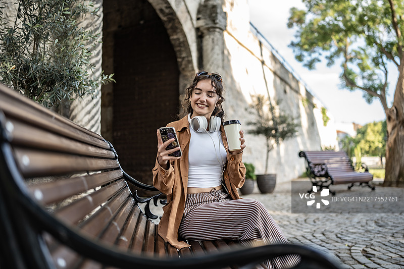 年轻女性在户外享受轻松的一天，手拿咖啡，戴着耳机图片素材