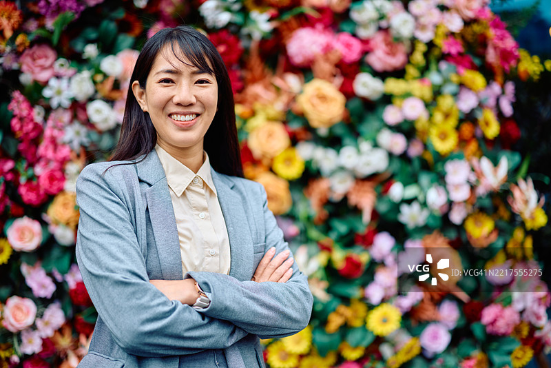 微笑的女商人双臂交叉，站在五彩缤纷的花墙前图片素材