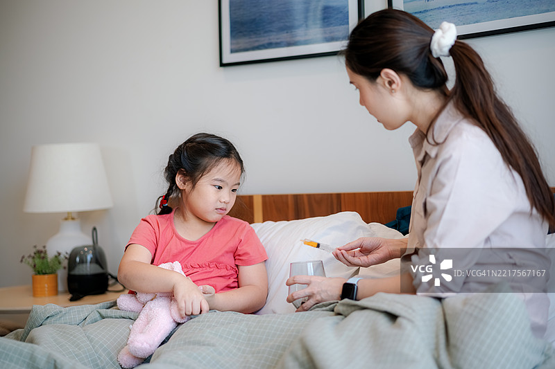 母亲正在用注射器给她的小女儿喂药。图片素材