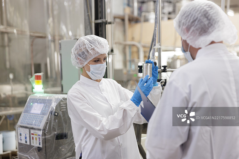 质量保证人员正在检查罐装产品并与同事讨论图片素材