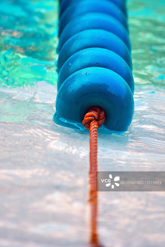特写镜头展示了一条蓝色泳道隔离带漂浮在清澈的浅蓝色水中。图片素材