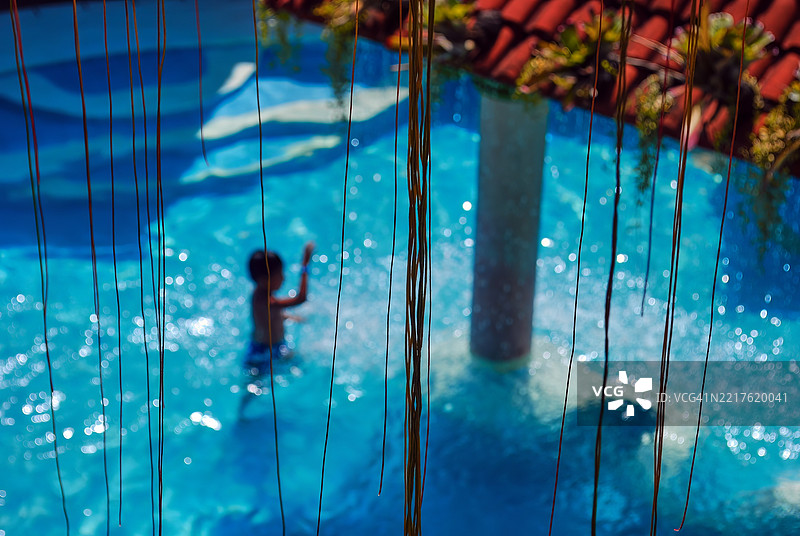 一个孩子在游泳池里，池底有蓝色波浪图案。图片素材