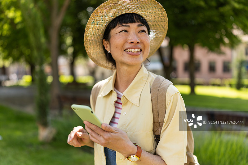 微笑的女性旅行者在城市公园使用手机图片素材
