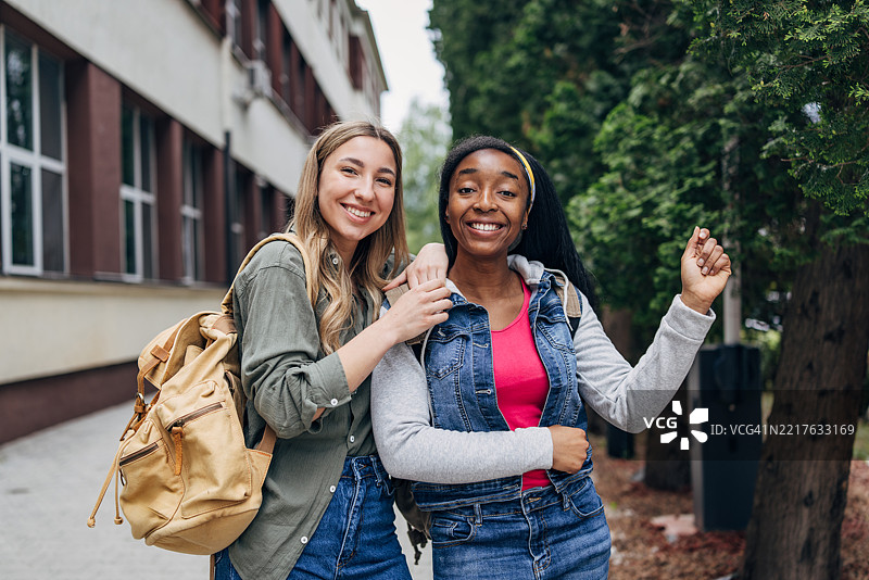 朋友们在大学建筑前享受阳光明媚的户外时光，一边学习一边快乐地在一起。图片素材