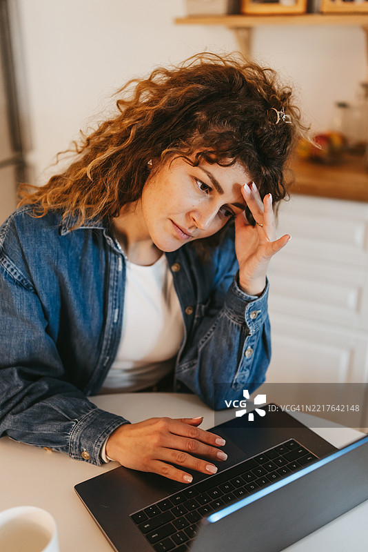 专注的女性坐在餐桌前，在家中使用笔记本电脑工作图片素材