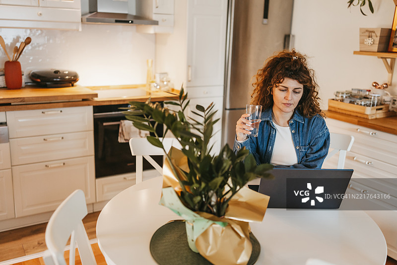 美丽的女人坐在餐桌旁，正在家中用笔记本电脑工作图片素材