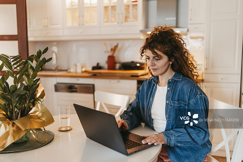 美丽的女人坐在餐桌旁，正在家中用笔记本电脑工作图片素材