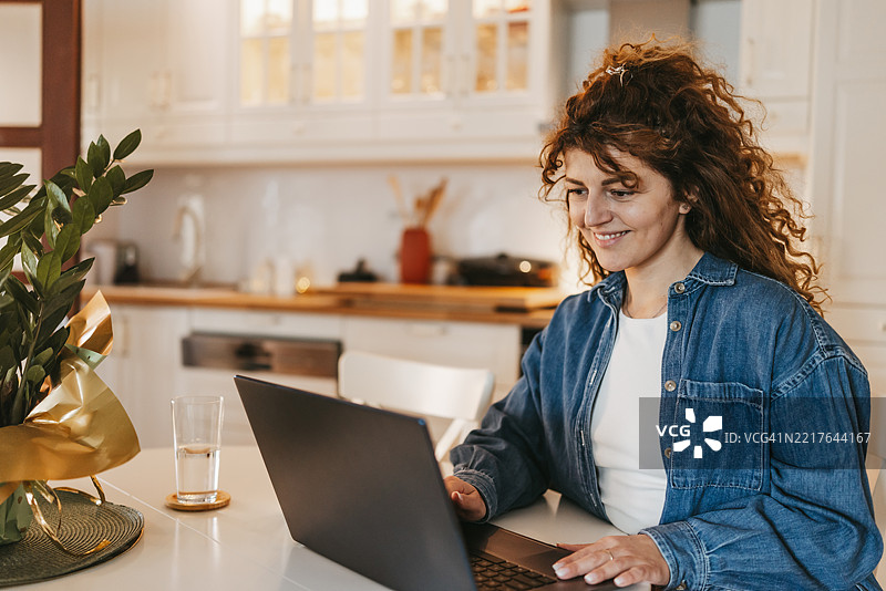美丽的女人坐在餐桌旁，正在家中用笔记本电脑工作图片素材