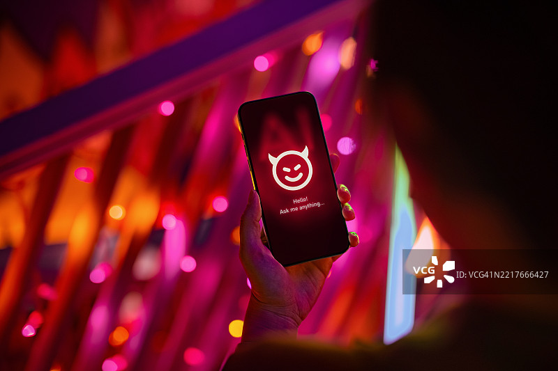 女性手持智能手机，屏幕上显示着带有恶魔角的邪恶形象，正在与AI聊天应用对话，背景为城市。展示了关于人工智能（AI）风险和危险的理念，以及对其影响的关注和谨慎考虑。图片素材