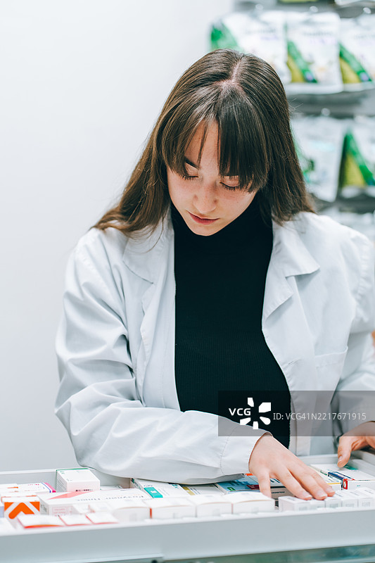 年轻的药剂师在药房抽屉中寻找药物图片素材