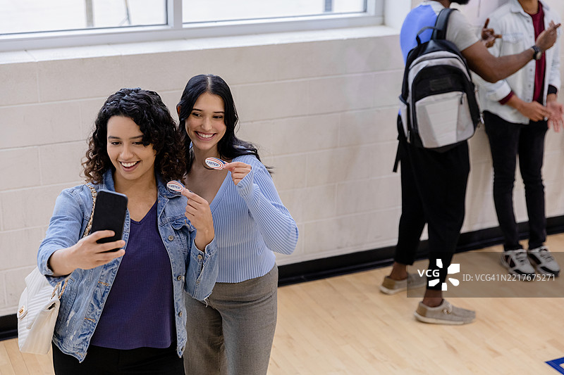 两位年轻女性微笑着，展示“我投票了”贴纸，自拍照图片素材
