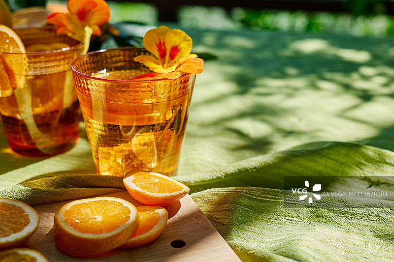 花园桌子上的冰镇花草水，加入可食用的金莲花和橙片。清爽的夏季饮品。健康的有机排毒苏打饮料。图片素材