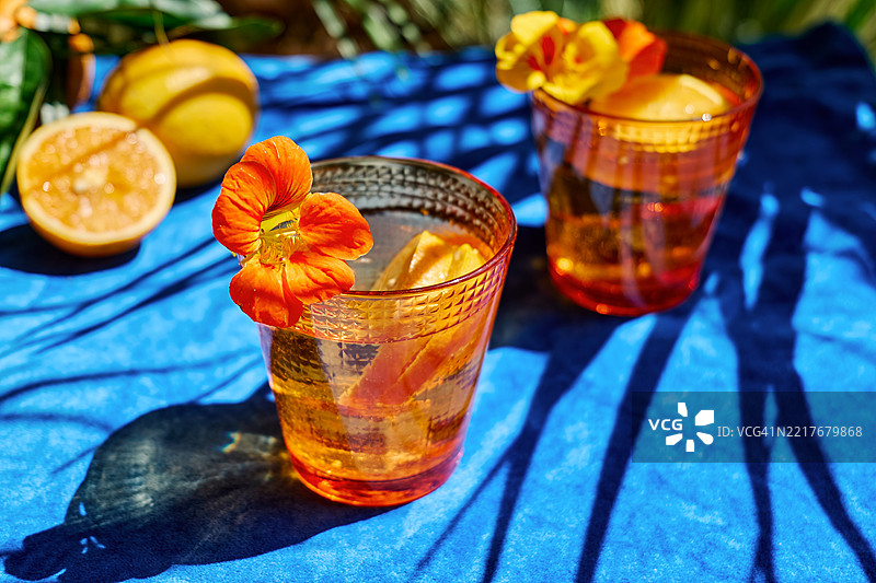 用可食用的金莲花和橙片装饰的冰镇水，放在热带花园的蓝色桌布上。清爽的夏季饮品。健康的排毒有机苏打饮料。图片素材