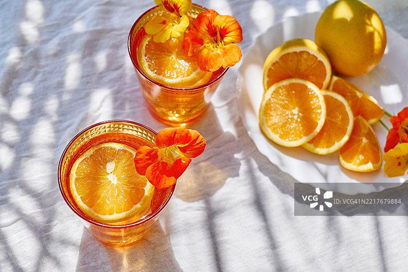 热带花园桌上的冰冻花草水，配有可食用的金莲花和橙片。清爽的夏季饮品。健康的排毒有机苏打饮料。图片素材