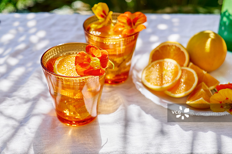 热带花园桌上的冰冻花草水，配有可食用的金莲花和橙片。清爽的夏季饮品。健康的排毒有机苏打饮料。图片素材