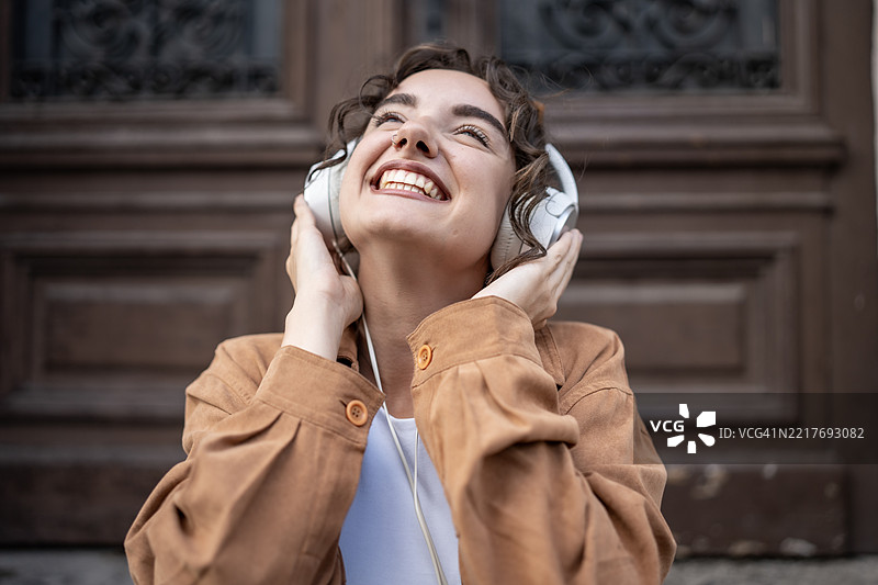 微笑的年轻女性在木门外戴着耳机享受音乐图片素材