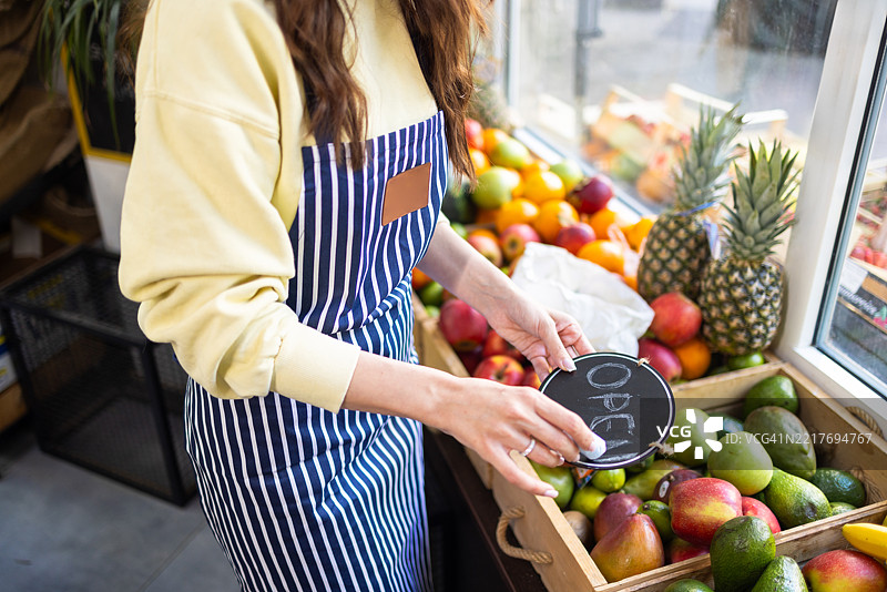 商店老板为她的杂货店准备“开门”标志。图片素材