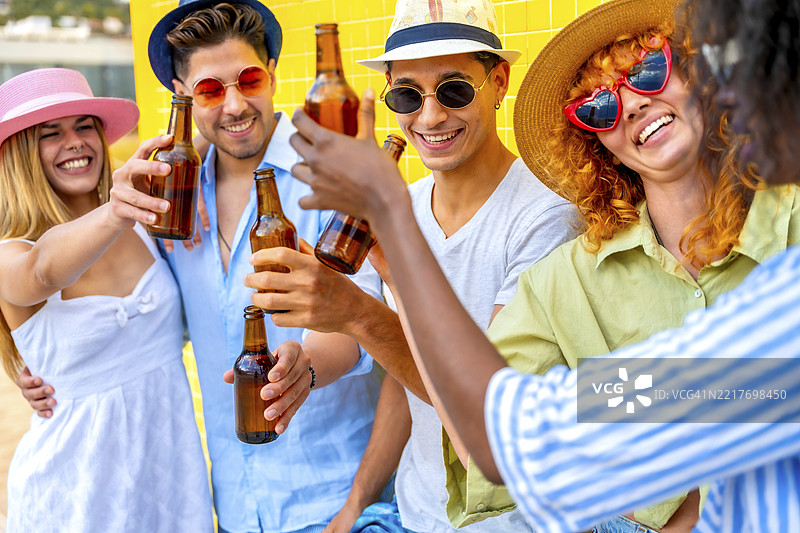 一群快乐的多种族年轻人穿着夏季服装和帽子，在夏季派对上举杯畅饮啤酒。图片素材
