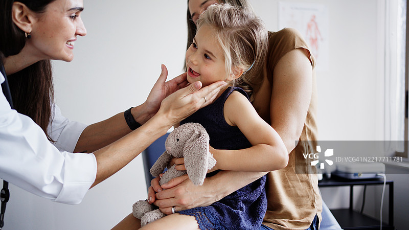 医生在诊所为年轻女孩检查颈部，母亲陪伴在旁。图片素材
