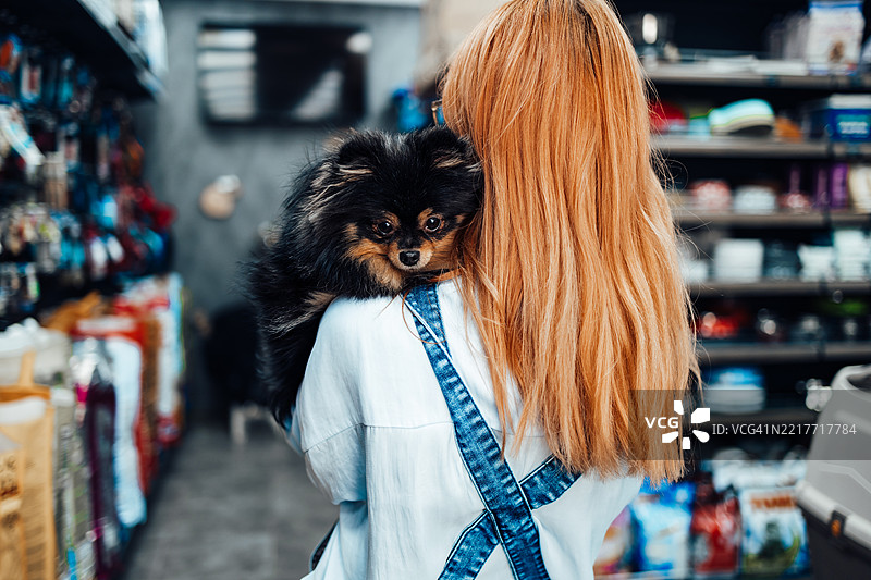 女人在宠物店里抱着博美犬：购物用品图片素材