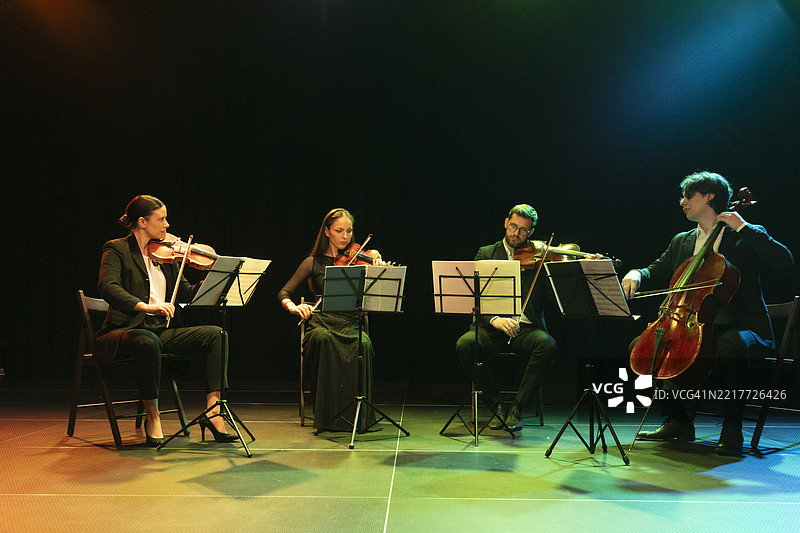 穿着正式服装的弦乐四重奏成员在剧院舞台上享受着他们在观众面前的表演图片素材