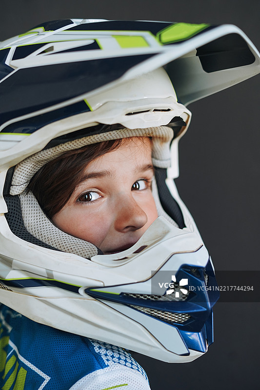 6-7岁男孩佩戴摩托车头盔的肖像，背景为深色图片素材