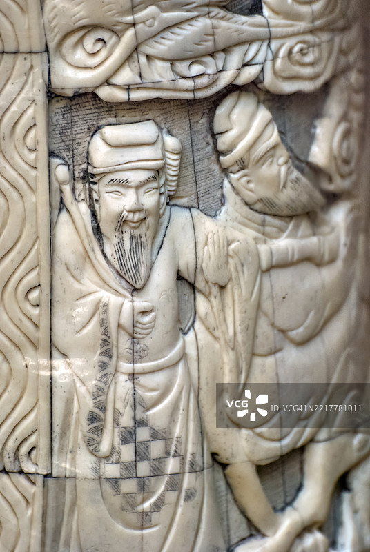 一件雕刻的象牙作品，描绘了两位身着传统服饰的人物，细致的图案和生动的面孔。图片素材