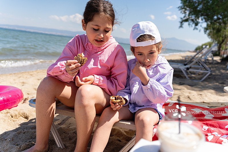 两个年轻的姐妹在阳光明媚的海滩上一起享受零食图片素材