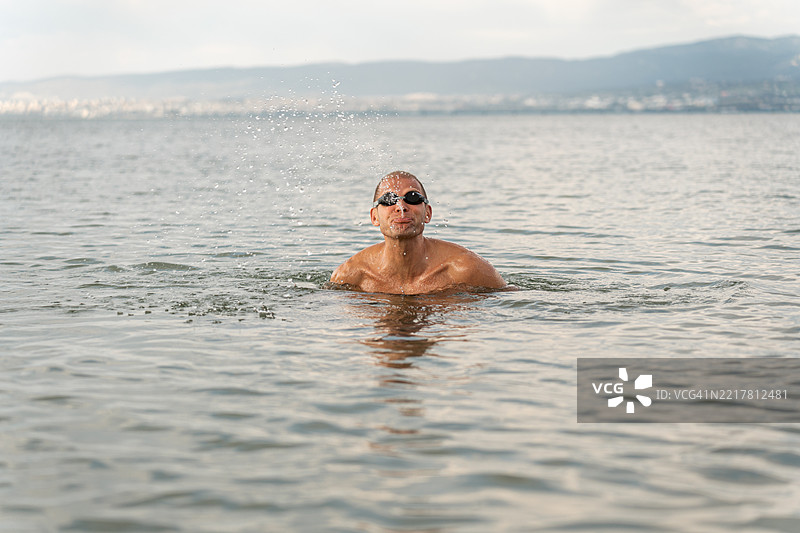 一个男人在阳光明媚的日子里在宁静的湖中游泳图片素材