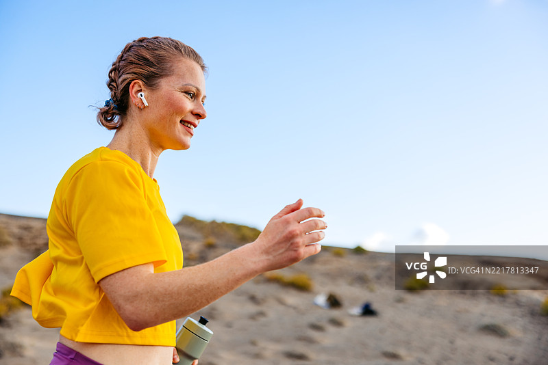 年轻女性在西班牙特内里费岛慢跑时听音乐并手持水瓶图片素材