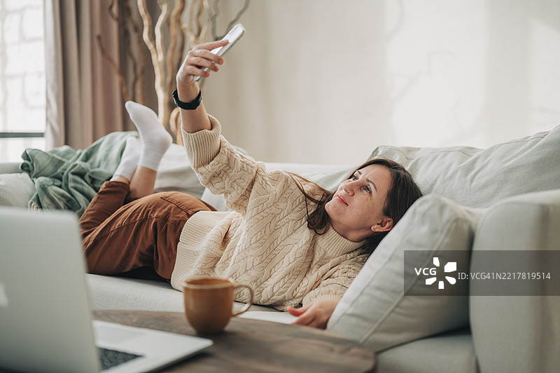 年轻女性在家沙发上躺着使用手机图片素材