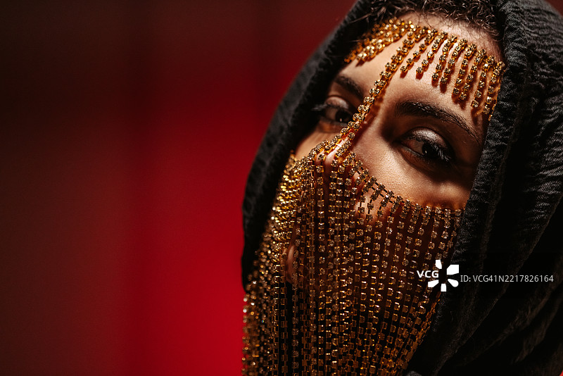 年轻女性佩戴中东风格面具，黑色兜帽在红色霓虹灯下照耀图片素材