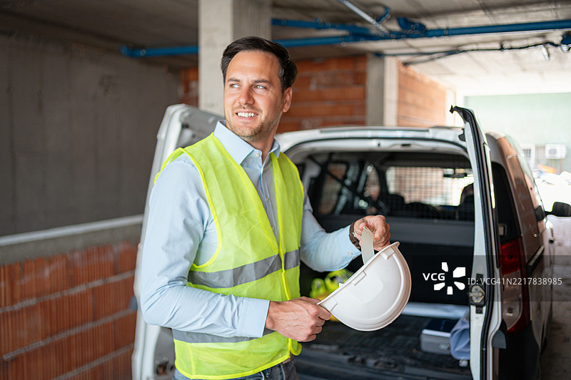 穿着高可视性背心的工程师在建筑工地上手持安全帽图片素材