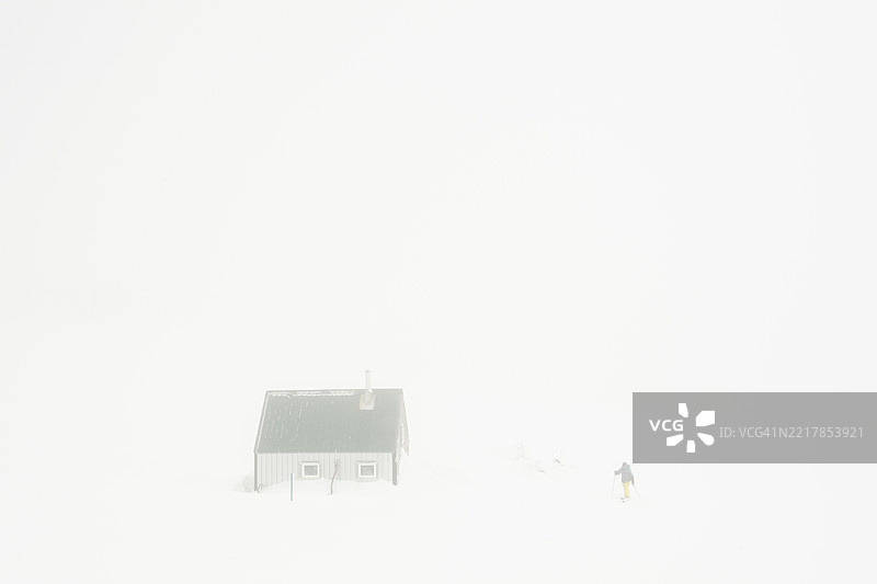 雪暴中男子与山间小屋的鸟瞰图图片素材