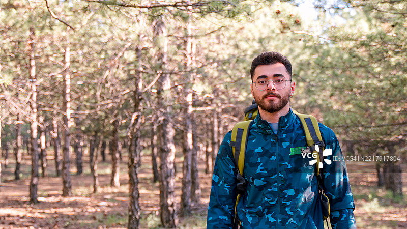 阳光明媚的日子里，男子在松树林小径上徒步旅行图片素材