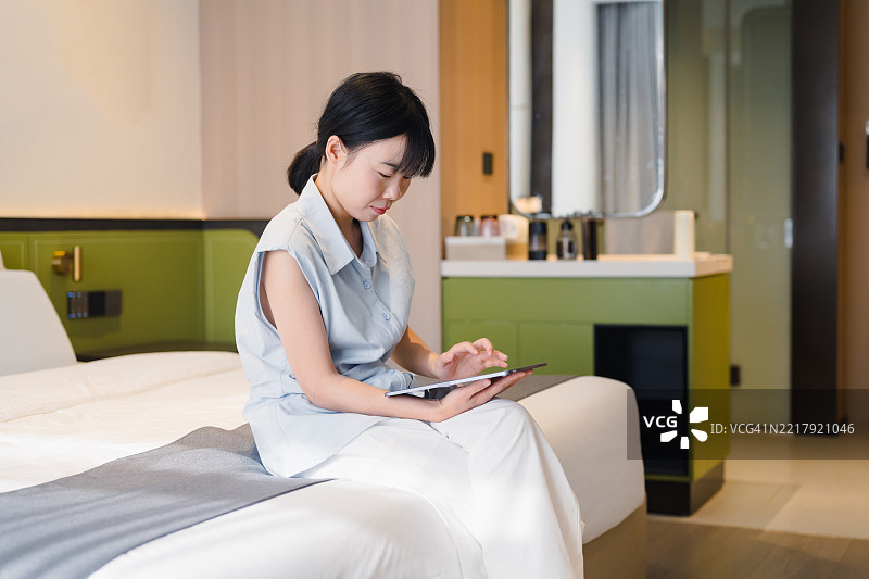 城市年轻女性坐在酒店床上使用iPad图片素材