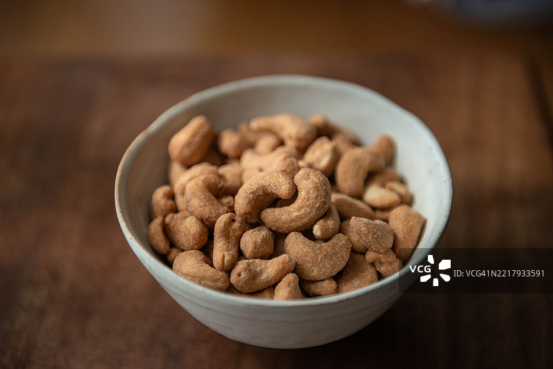 一个高角度特写的碗里装满了腰果，放在木桌上；腰果提供健康脂肪、蛋白质和必需矿物质。图片素材