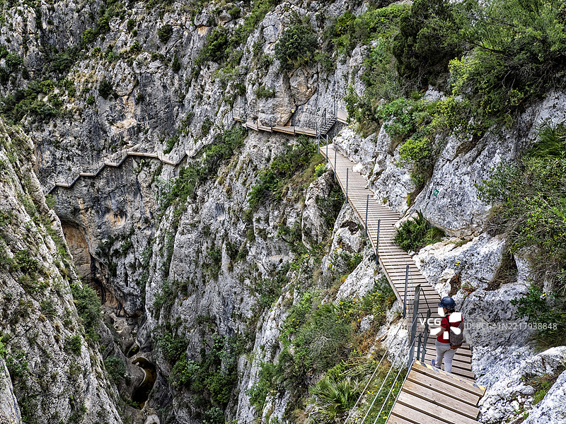 一位女性在大峡谷的岩壁之间的木栈道上徒步行走，雷尤桥（Pasarela de Relleu）图片素材