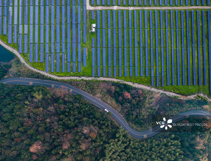 高角度视图的太阳能电池板，蜿蜒道路上的汽车与五彩斑斓的森林图片素材