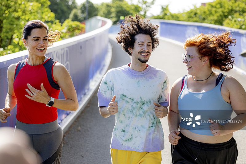 三位朋友在城市公园清晨一起跑步，展现多样性。图片素材