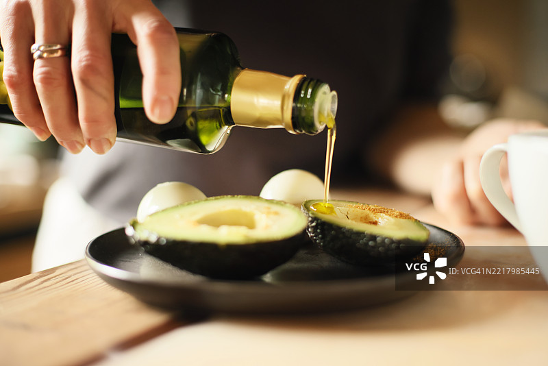 盘子上放着淋有橄榄油的鳄梨和水煮蛋，桌子是石头和木材制成的。图片素材