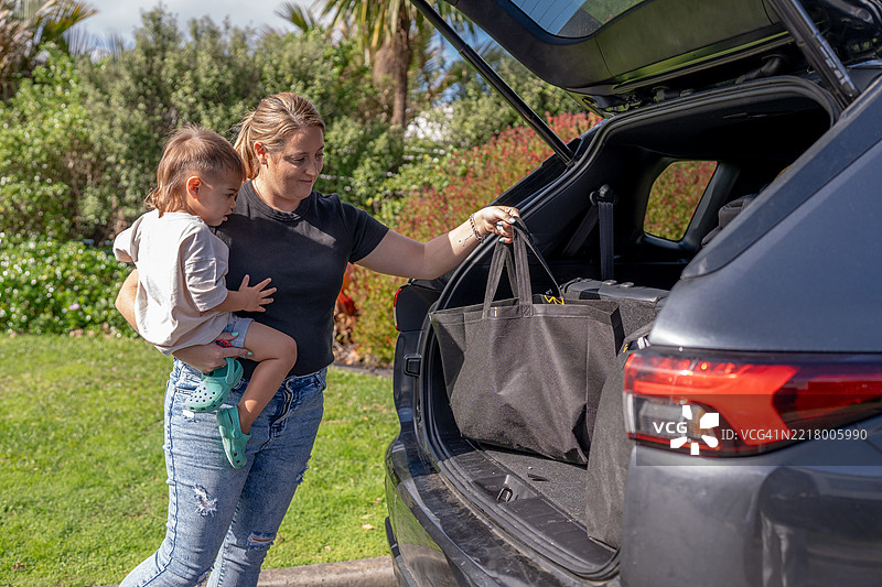 母亲在卸载汽车后备厢时抱着孩子图片素材