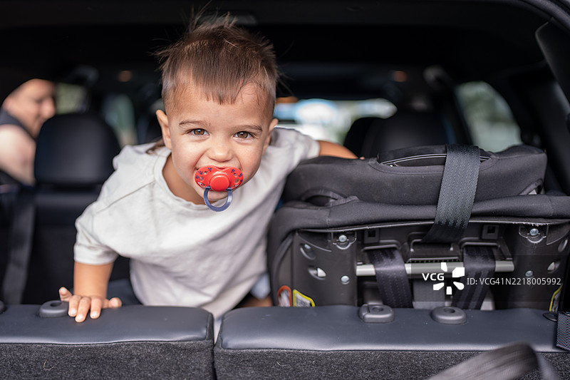 幼儿靠在汽车后备箱上，嘴里含着安抚奶嘴图片素材