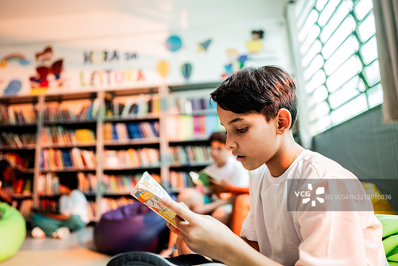 学校图书馆里的小男孩在阅读漫画书图片素材